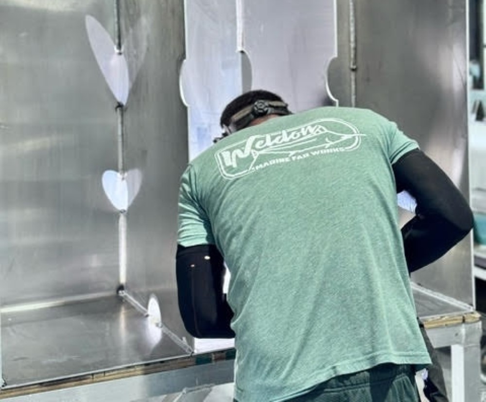 the back of a man bending over a marine fuel tank wearing a weldon marine fabworks shirt